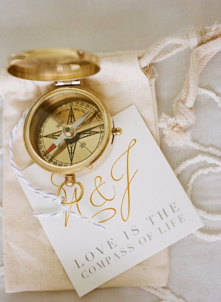 A gold compass travel wedding favor is fitted with a tag that reads, "Love is the compass of life."