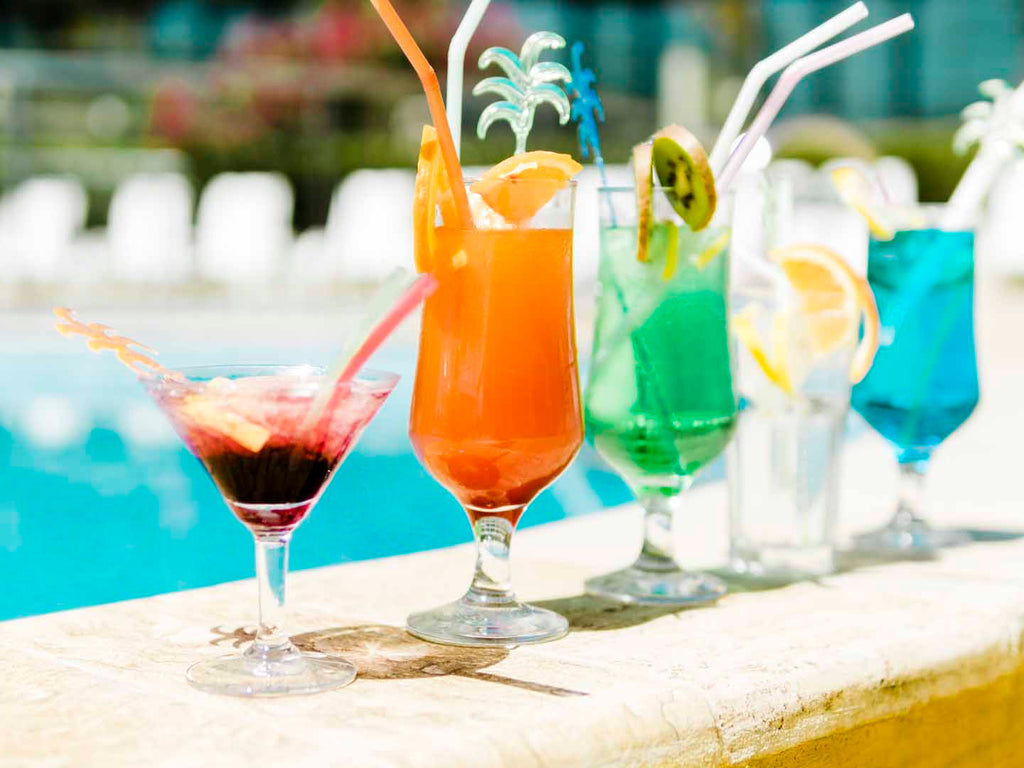 Four colorful cocktails sit on the ledge of a pool at a poolside wedding reception.