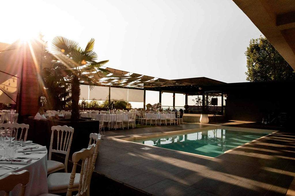 Elegant simple pool wedding setup with pool in the middle of the venue, surrounded by set, white tables at sunset.