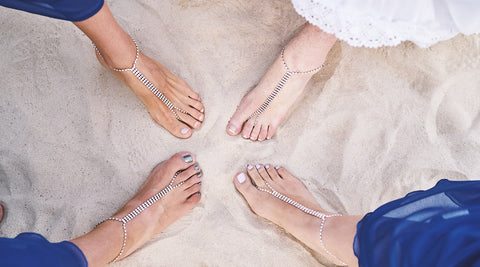 The feet of a bride and bridesmaids are shown displaying their jeweled, thong flip-flops against the sand. 