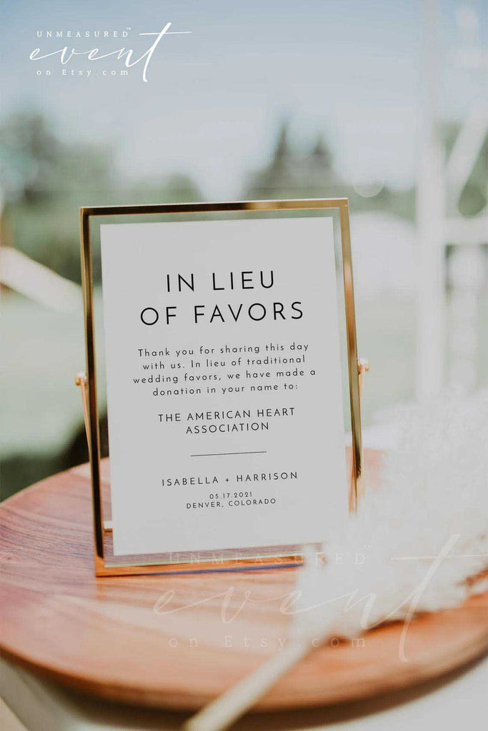 A card that reads, "in lieu of favors" rests on a small wooden table with a white feather. 