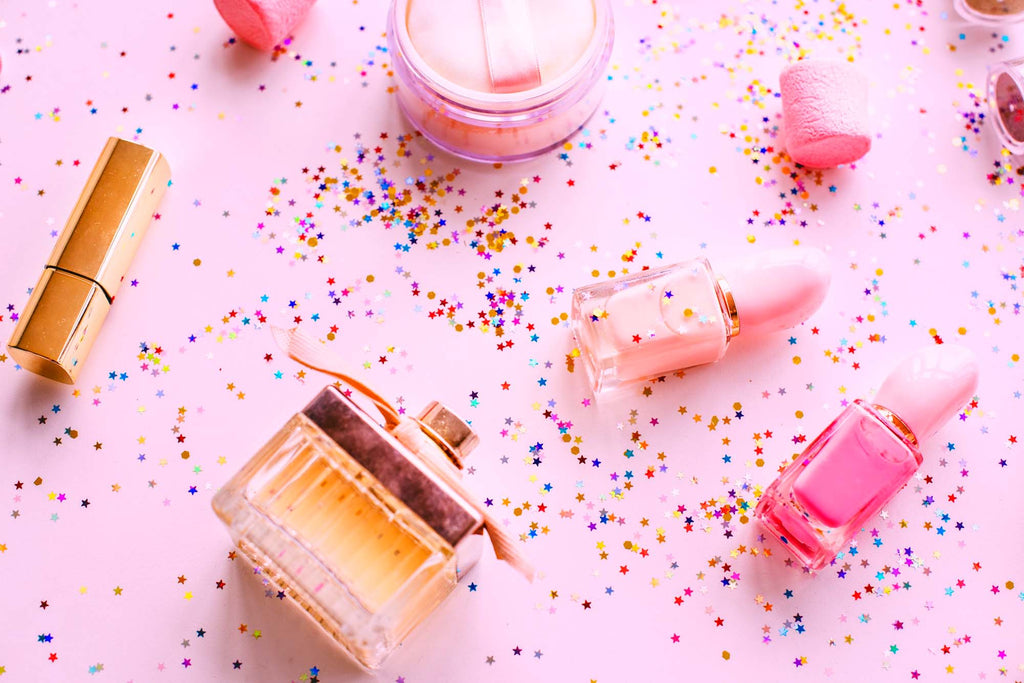 Lip balm, perfume and nail polish are laid out on a pink background with colorful spots.  