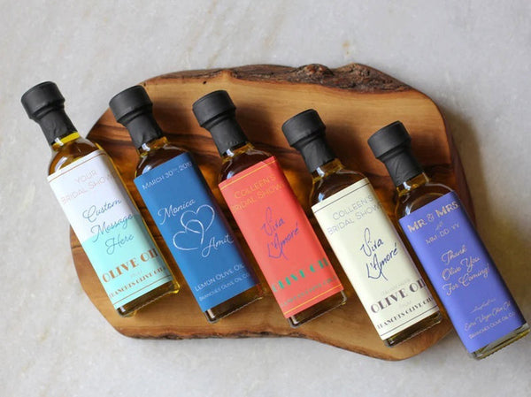 5 custom label olive oil boho wedding favor bottles rest at a diagonal on a burn stripped cutting board.