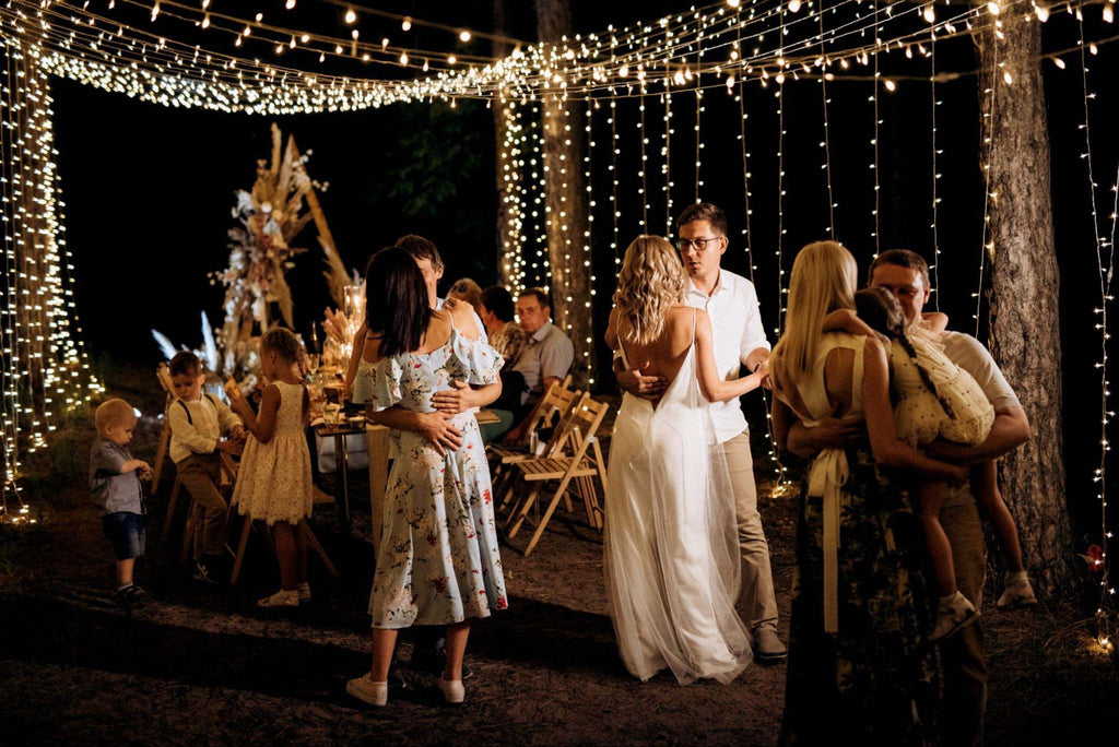 Wedding guests dance and play at an outdoor nighttime wedding reception decorated with fairy lights.