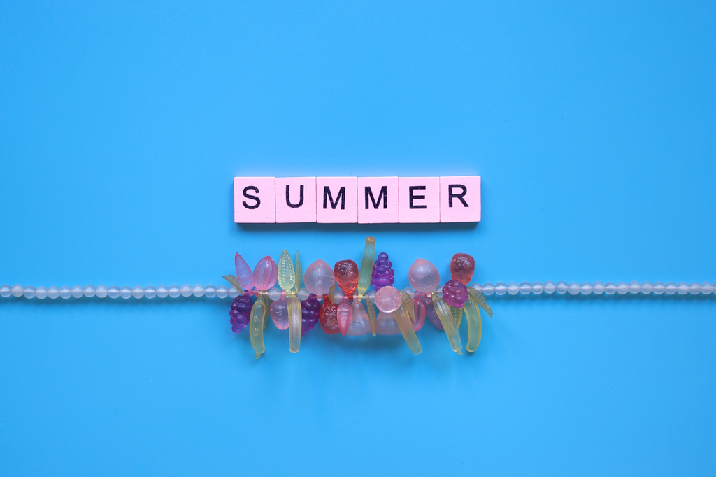 A string of tiny white beads is fitted with colorful translucent fruit charms to make a pool party favor. The word summer is written above the bracelet in Scrabble tile letters.