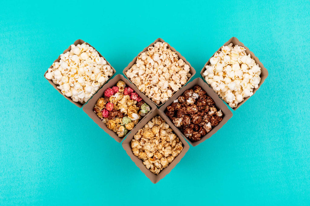 6 different brown snack boxes are filled with 6 different flavors of popcorn that are lined up in the shape of a heart.