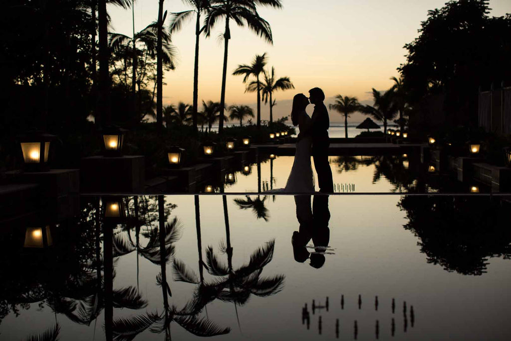 Wedding by the pool with silhouettes of the bride and groom reflecting in the water at sunset.