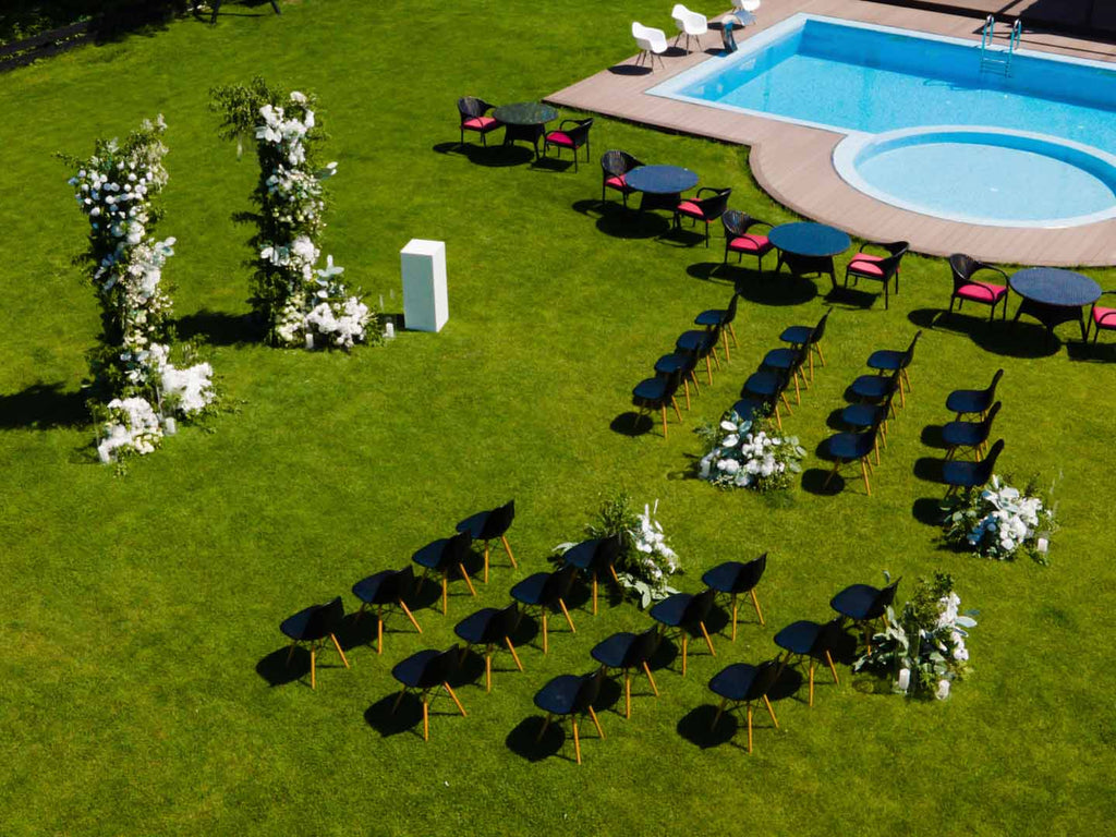 Poolside wedding with bridal arch, with white flowers and greenery and black chairs for guests