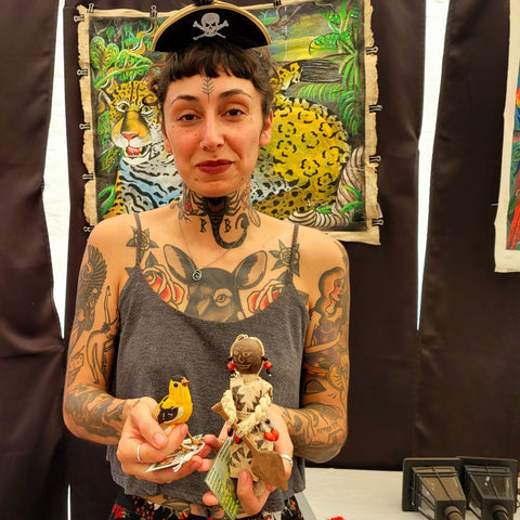 Woman with nature tattoos buying bird and Yagua doll at Amazon Ecology booth at Grey Fox Bluegrass Festival