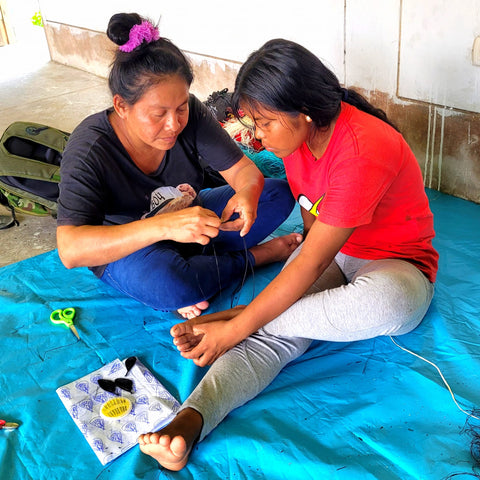 Doilith showing young artisan to weave chambira butterfly at Amazon Ecology workshop