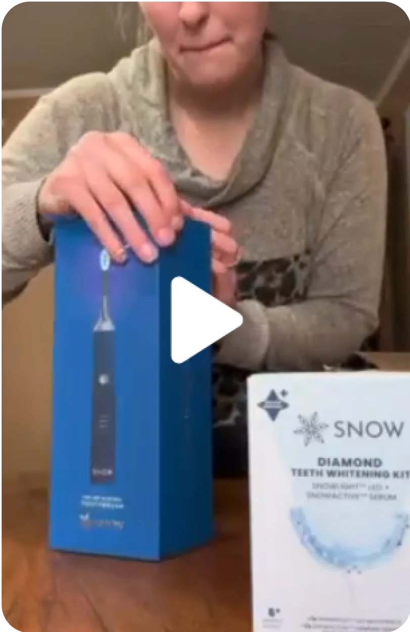 Person demonstrating a blue electric toothbrush and a Snow teeth whitening kit.