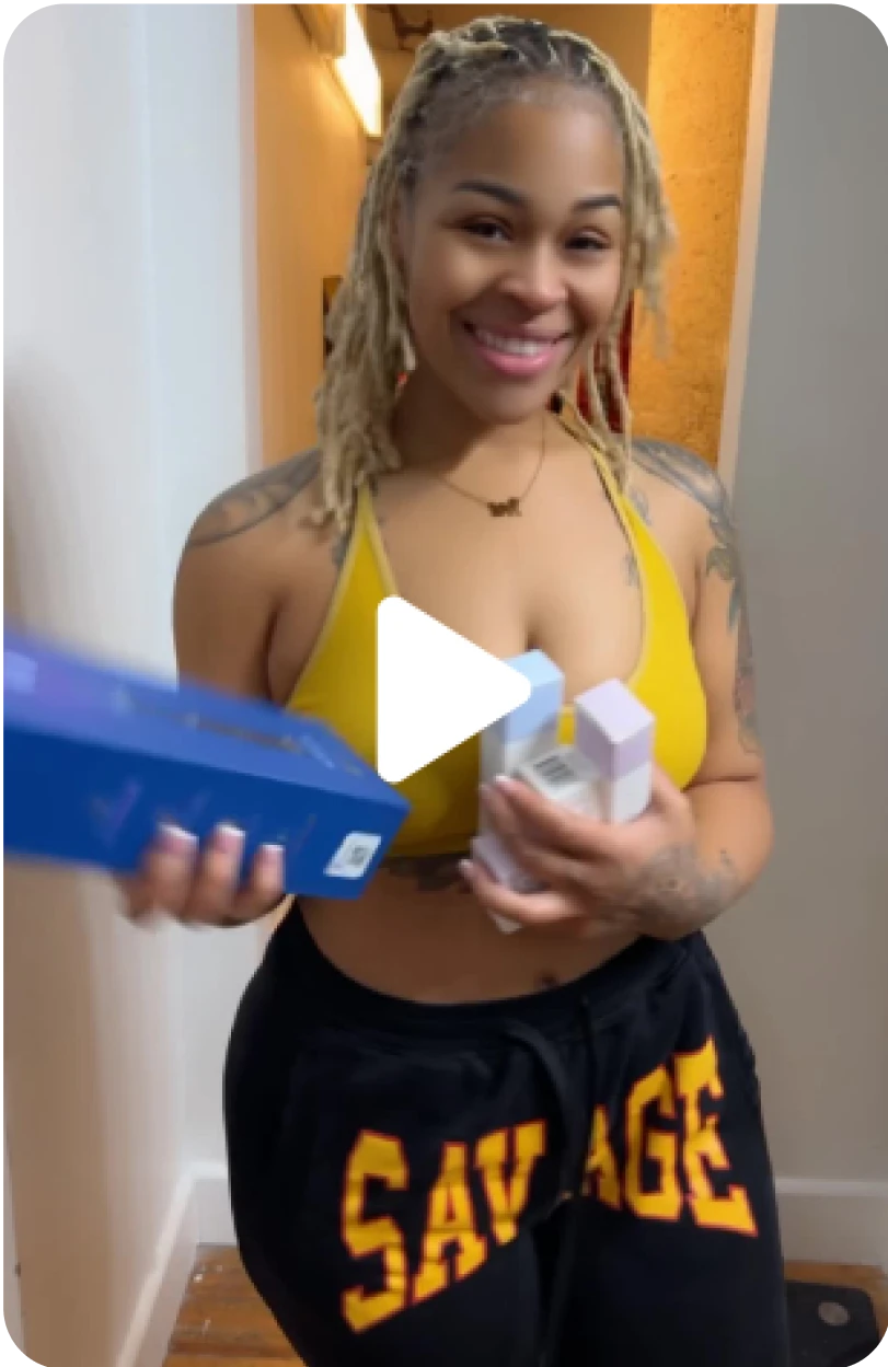 Smiling woman in a yellow top holds various boxed products, wearing 'SAVAGE' pants.