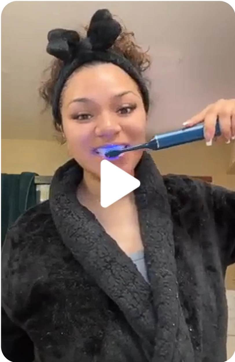 Person in a robe brushing their teeth with an electric toothbrush that has a blue light.