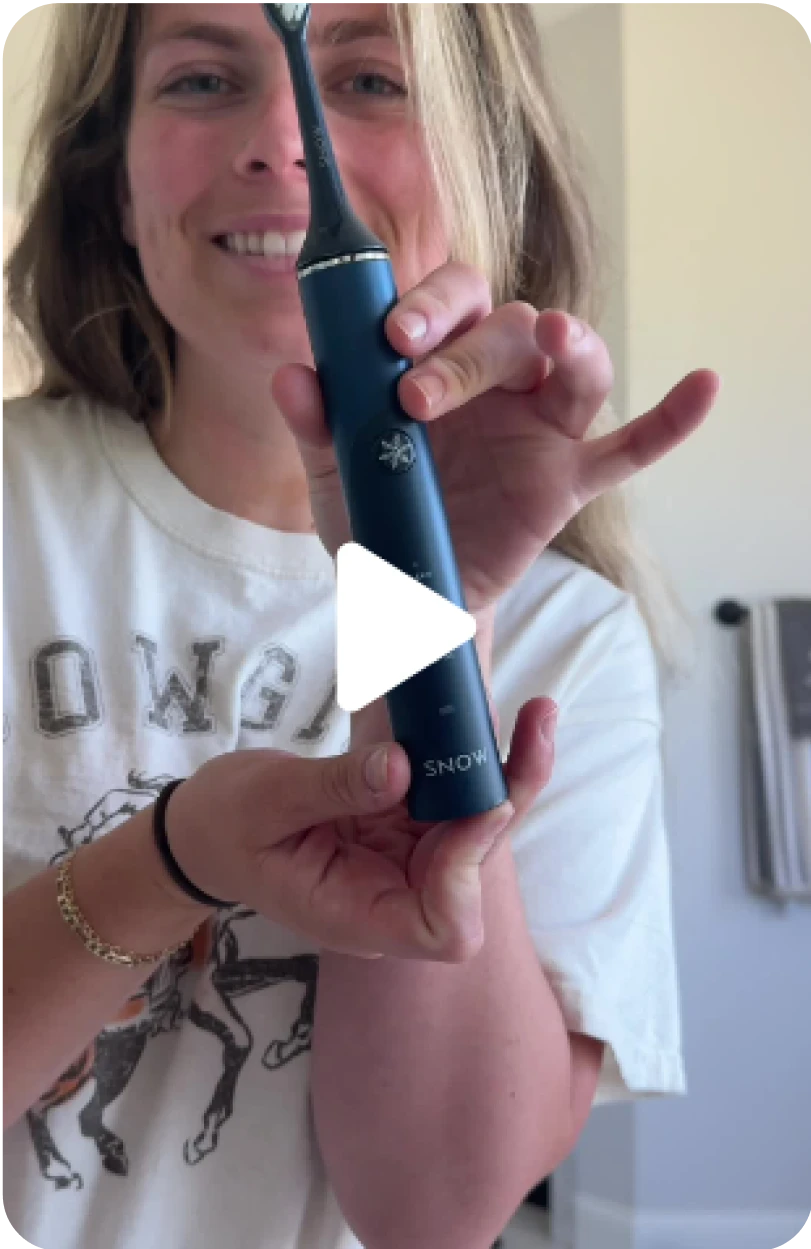 Person holding a blue electric toothbrush, smiling.