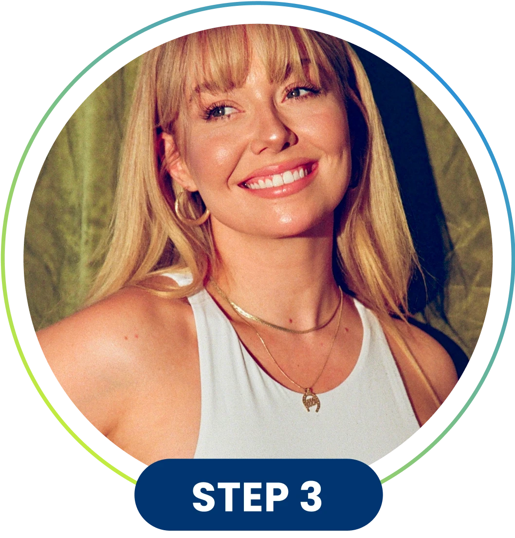 Smiling woman with blonde hair and bangs, wearing a white top and gold jewelry.