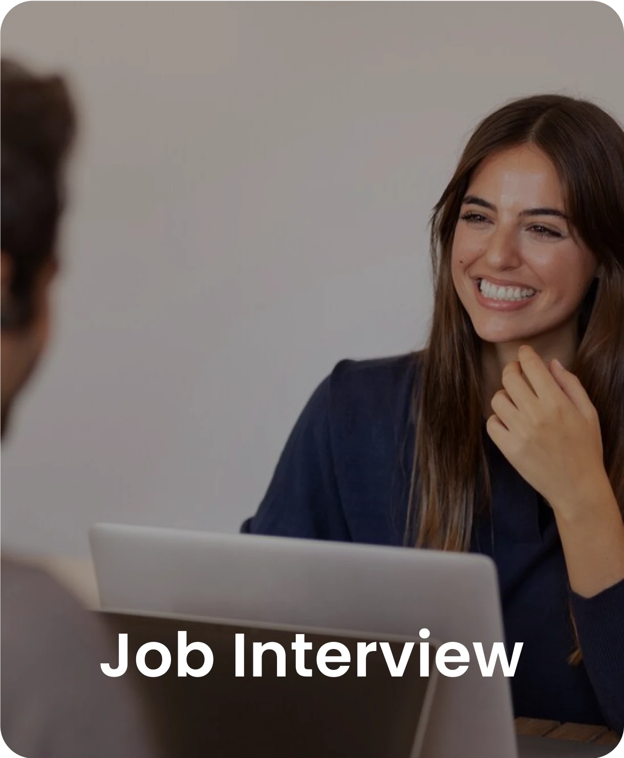 A woman smiling during a job interview, sitting at a desk with a laptop.