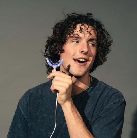 Man with curly hair holding a snow teeth whitening tray