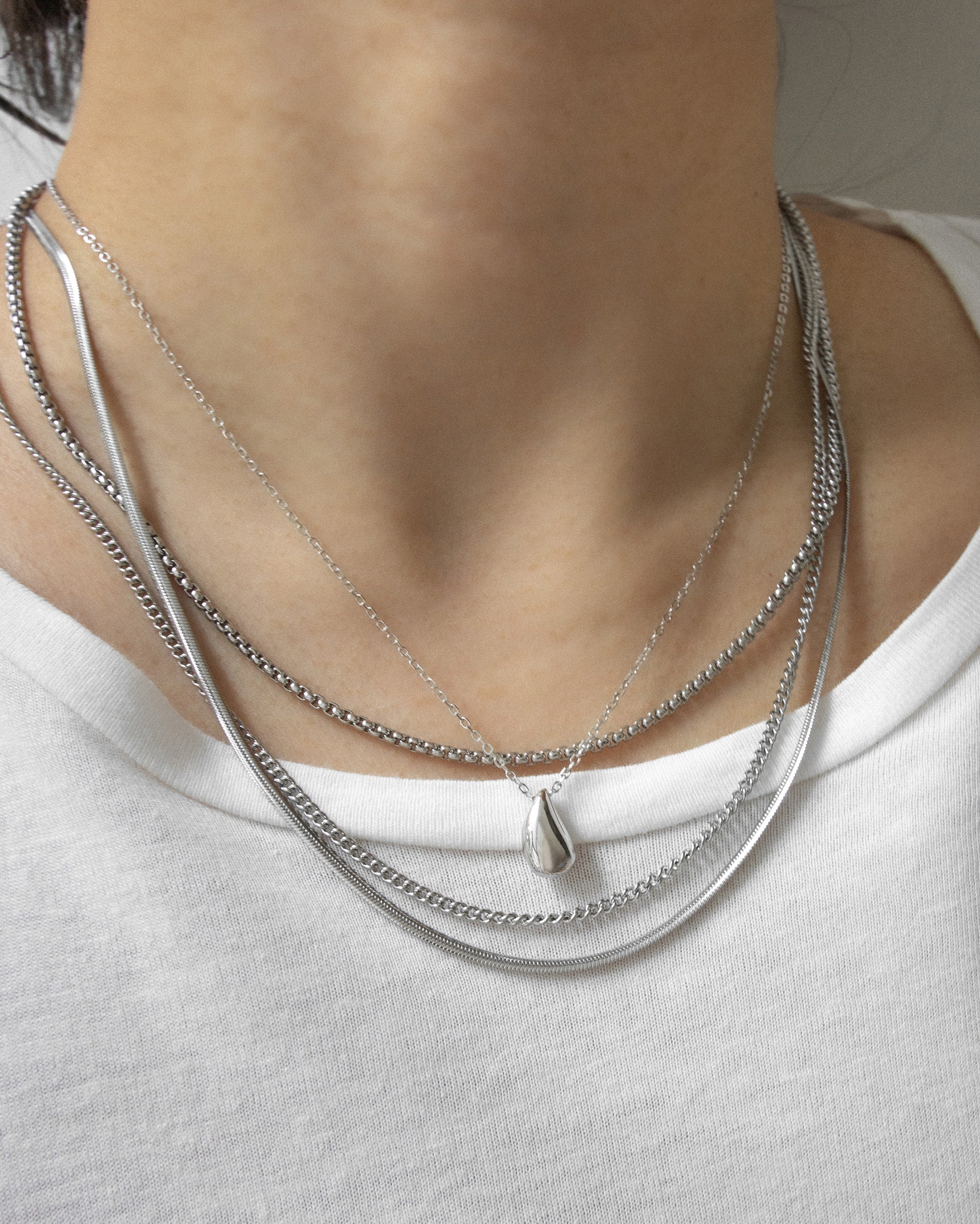 Silver teardrop pendant necklace anchors the neck stack for a cohesive look