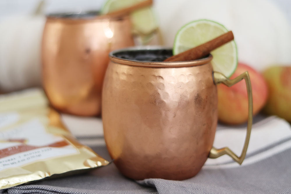 Two copper Moscow Mule cups in fall seasonal decor with apple cider mule cocktails