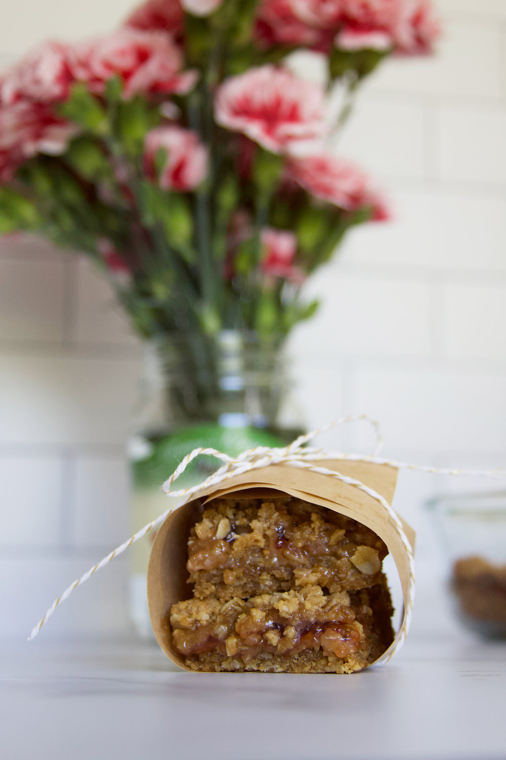 Peanut butter and jelly bars wrapped in paper with pink carnations in a Raven's Nest jar