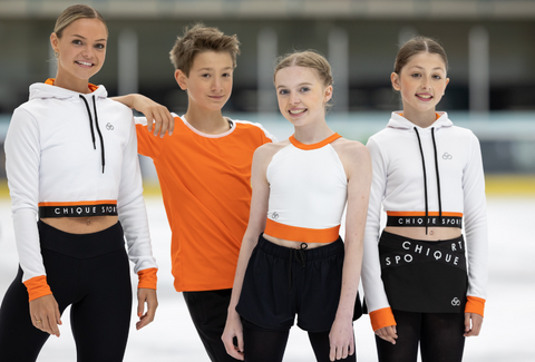 Group of four figure skating athletes posing for a photo on an ice rink, wearing Chique Sport activewear.