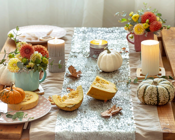 Summerween indoor table setting with white pumpkins, fresh flowers, candles, and halved squash arranged along a silver and beige table runner.