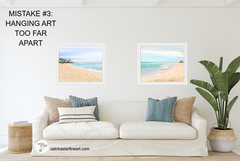 A couch with two beach photographs awkwardly hung too far apart.