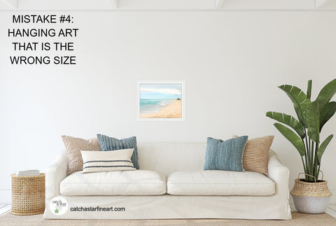 A white couch in a room with tropical accents. Above the sofa is a tiny beach photo that is too small for the space.