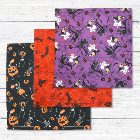 Three Halloween bandanas, one purple with ghosts, another orange with halloween designs and a black bandana with skeletons