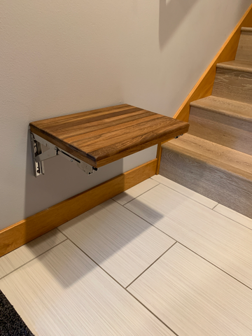 Folding wall mount bench mounted at the bottom of stairs by a door to use as a seat to put on or take off shoes.