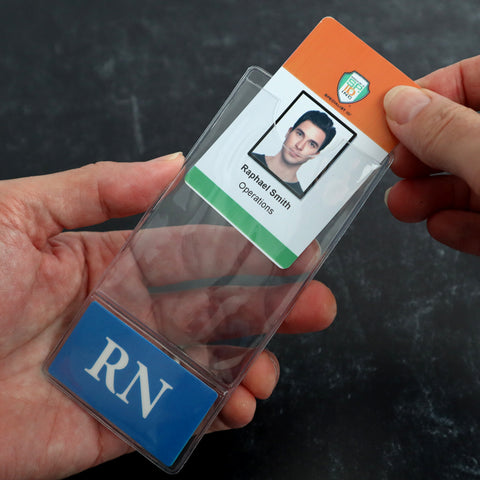 A close-up shows two hands handling an identification badge. The Custom Printed BadgeBottoms® Vertical (Badge Holder & Badge Buddy IN ONE!!) features a photo, the name "Rafael Smith," and the word "Operations." It is being inserted into a plastic holder with a blue section labeled “RN.”