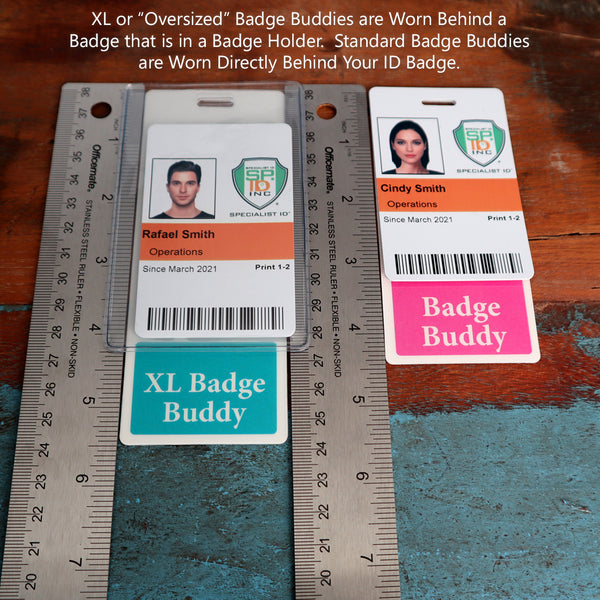 Two identification badges labeled for Rafael Smith and Cindy Smith are placed on a table beside rulers. Rafael's badge has a teal card below it labeled "Custom Printed Badge Buddy Vertical (Standard Size)," while Cindy's has a pink card labeled "Custom Printed Badge Buddy Vertical (Standard Size)." Text explanation is visible above, showcasing the custom badge buddies.