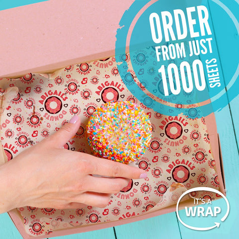 Image featuring a hand taking a sprinkle covered donut from a box which is lined with pink pattered greaseproof paper. Wording in the corner says "order from 1,000 sheets"