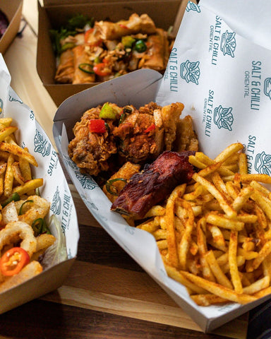 Take out boxes with fried chicken wings and fries. All feature a branded greaseproof featuring a green logo