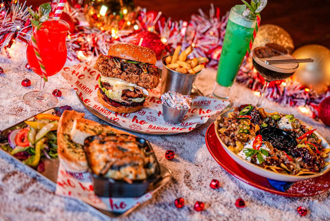 Table of food including burgers, pulled pork sandwiches and fries, all served alongside branded greaseproof paper with a red Christmas themed design.