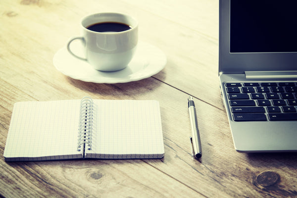 organised wooden desk including a coffee, a notepad, a pen, and a macbook