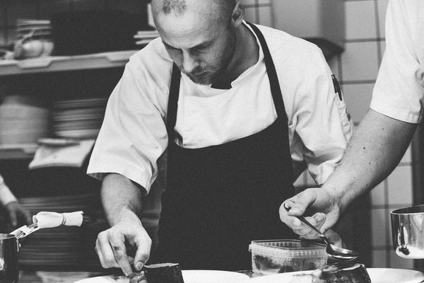 Jack Dusty Uniforms - Chef in chef jacket and apron garnishing his plate