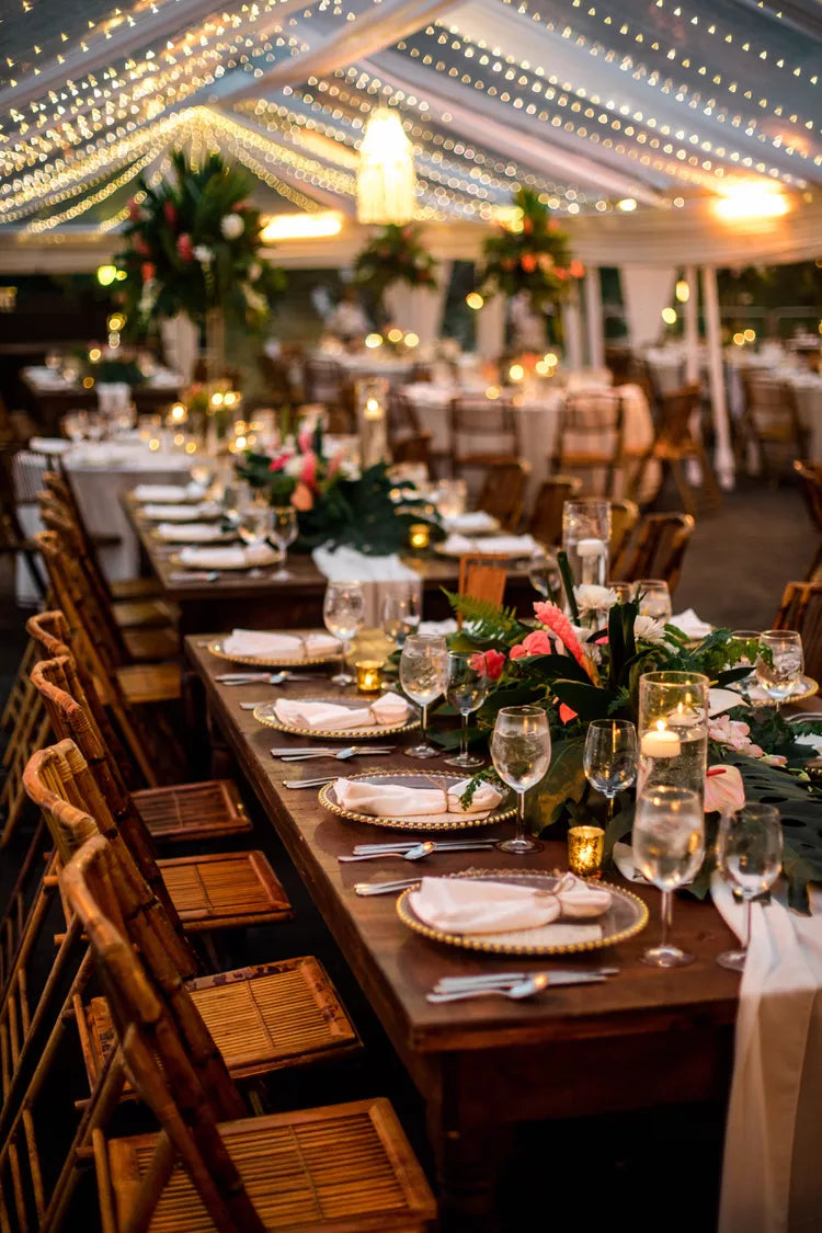 Close up of the table wedding decor. Rattan chairs, wooden tables and floral centerpieces made of monstera leaves.