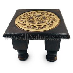An angled top-down view of a dark brown altar table. On top is a carved relief of a pentagram surrounded by swirls, and that has been painted gold.