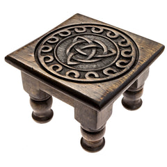 Angled top-down view of a dark brown wooden table. On the top of is a relief carving of the Triquetra 