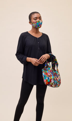 Standing woman wearing facemask made of patchwork African print fabric and carrying matching hand bag