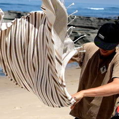 Man with EKZO shirt and hat shaking brown striped towel on the beach
