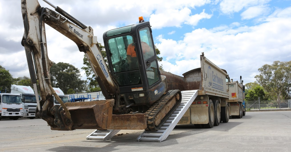 Heavy construction machine unloading a ute on a pair of aluminium loading ramps