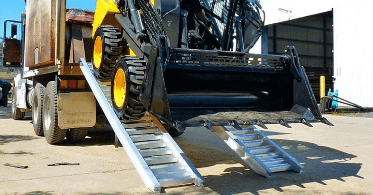 Big excavator using a pair of aluminium ramp to unload a truck 