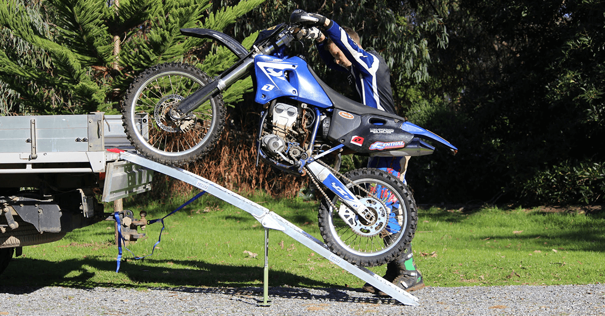 A motorcycle is being pushed to the truck using the ramp