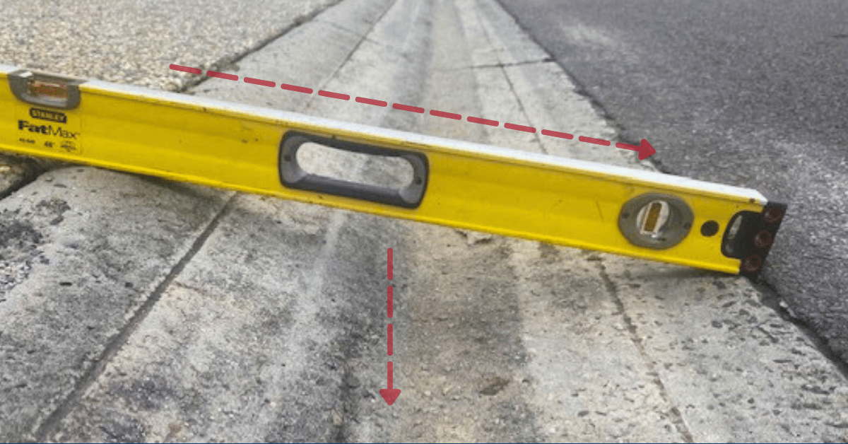 image shows a yellow level on a road. The level is placed in the center of the frame, and it has black markings along its length. It appears to be made out of metal, with a handle at one end for easy carrying.