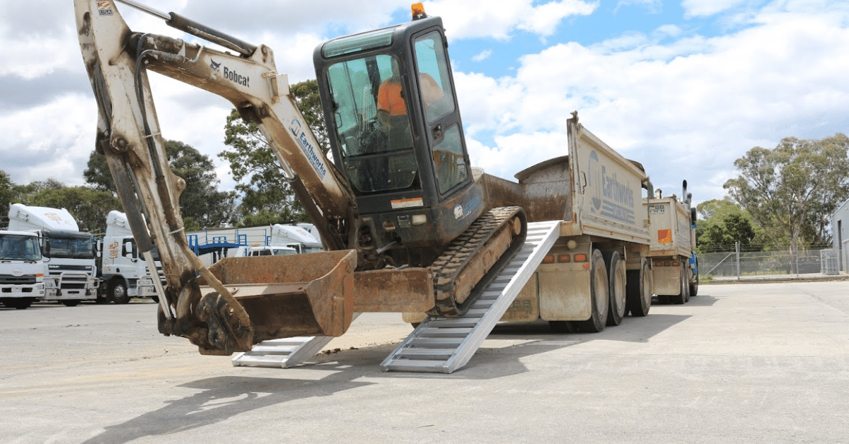 An excavator unloading a ute using a pair of construction machinery loading ramps
