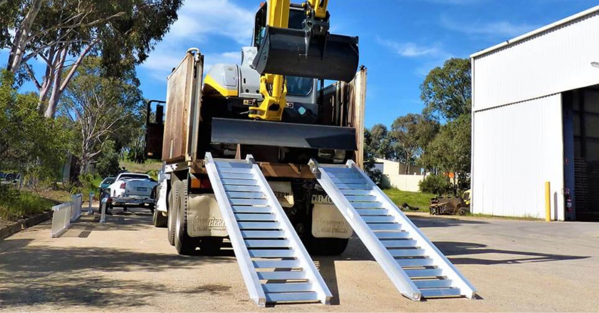 Image of machinery loading ramps attached at the rear of a truck with an excavator ready to unload