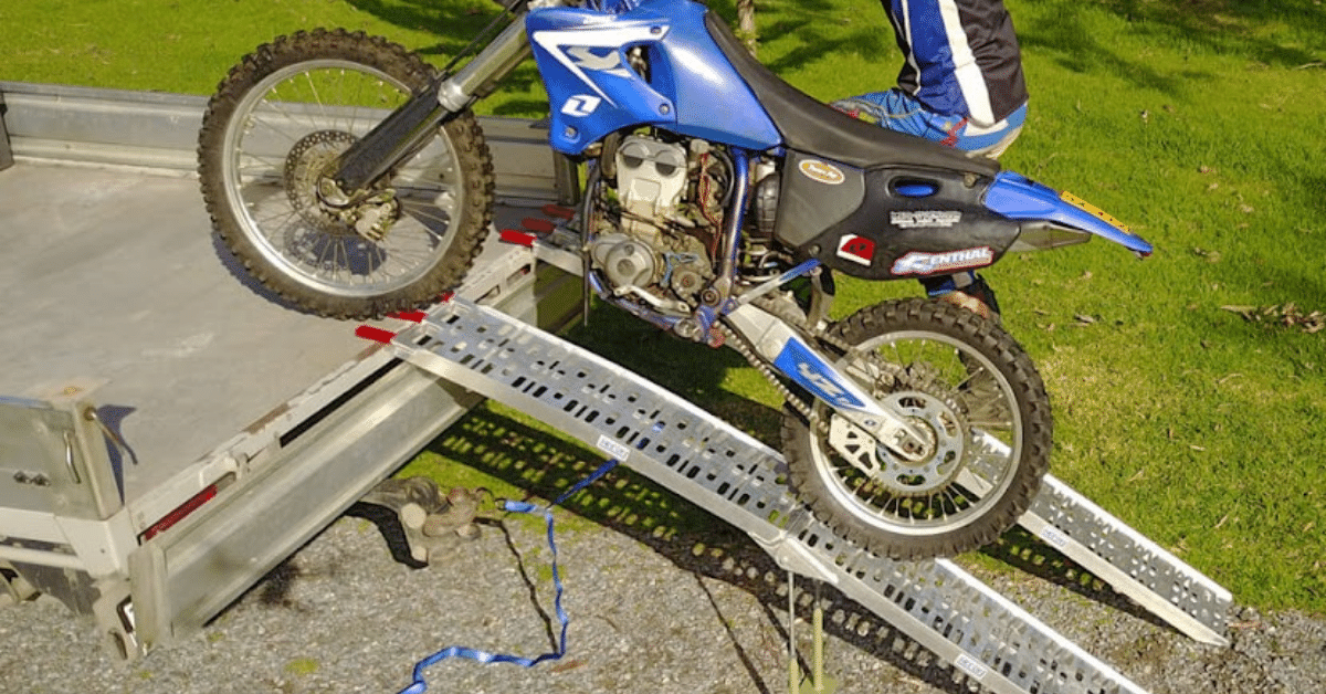 A man loading a motorcycle on a ute with a pair of aluminium ramp