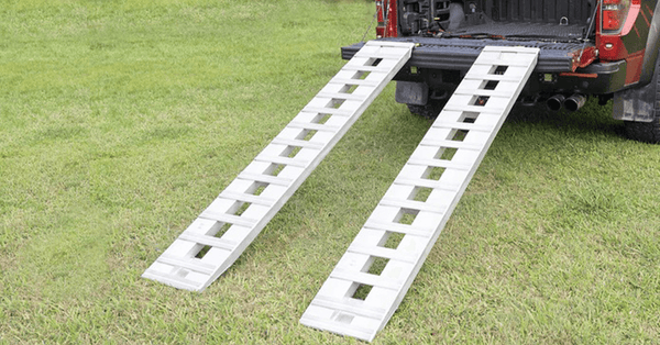 Set of aluminium ramps against a black ute parked on green grass